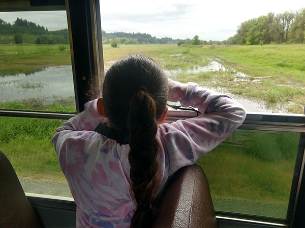 a student uses binoculars to search for birds out the bus window