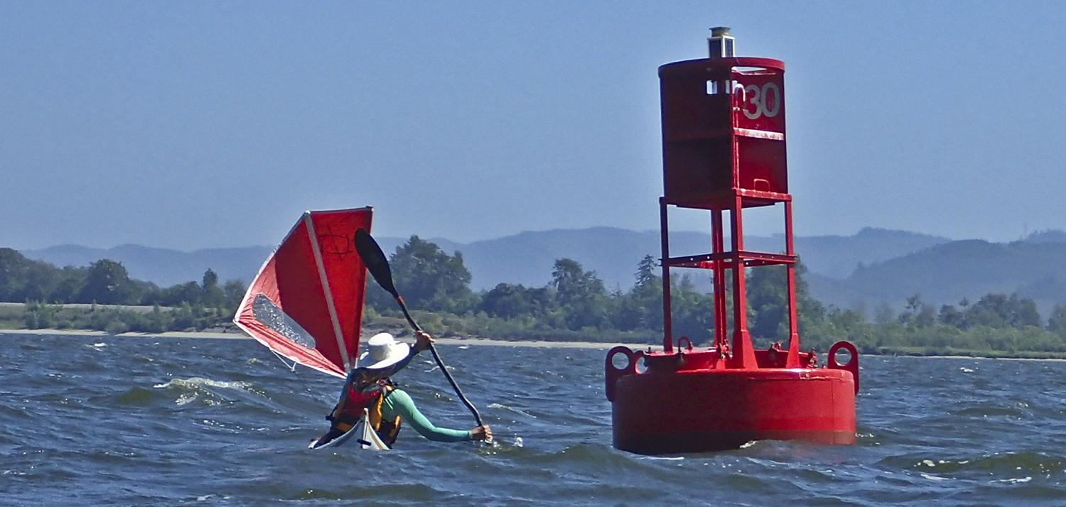 Ginni rides the wind and waves around a buoy in her kayak with windsail