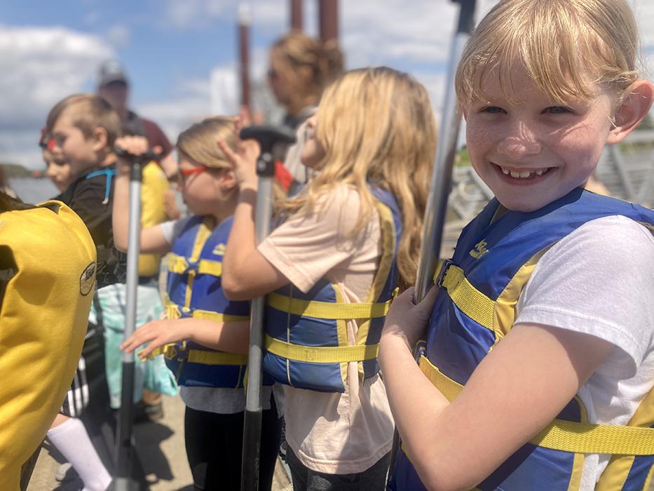 student wears a lifejacket and smiles, eager for a canoe paddle