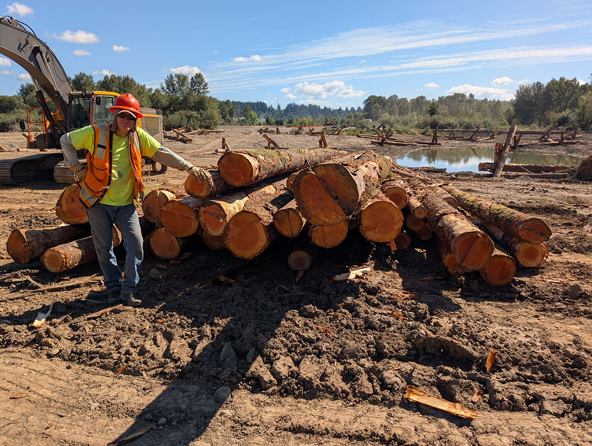 a worker in protective gear stands next to a pile of logs