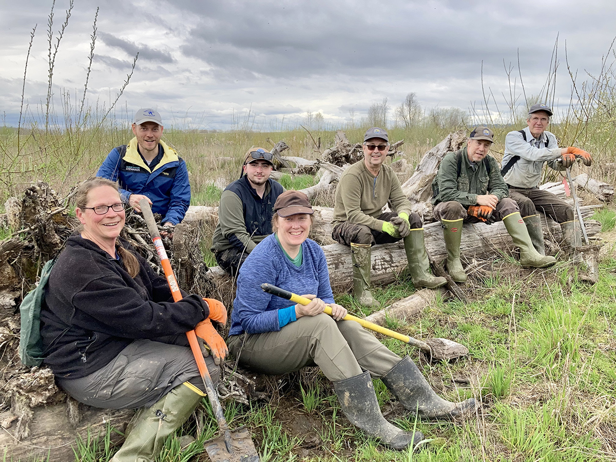 Seven folks sit on a log and smile