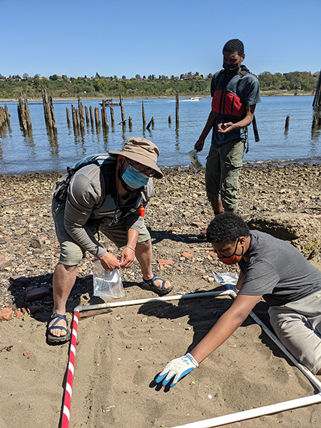 young man searches a plot in the sand for microdebris while an instructor looks on
