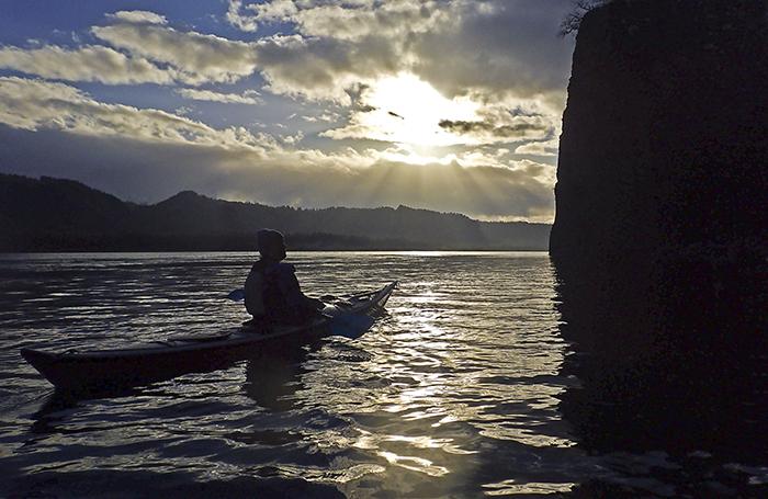 Kayaker silhouette with a setting sun by Cape Horn
