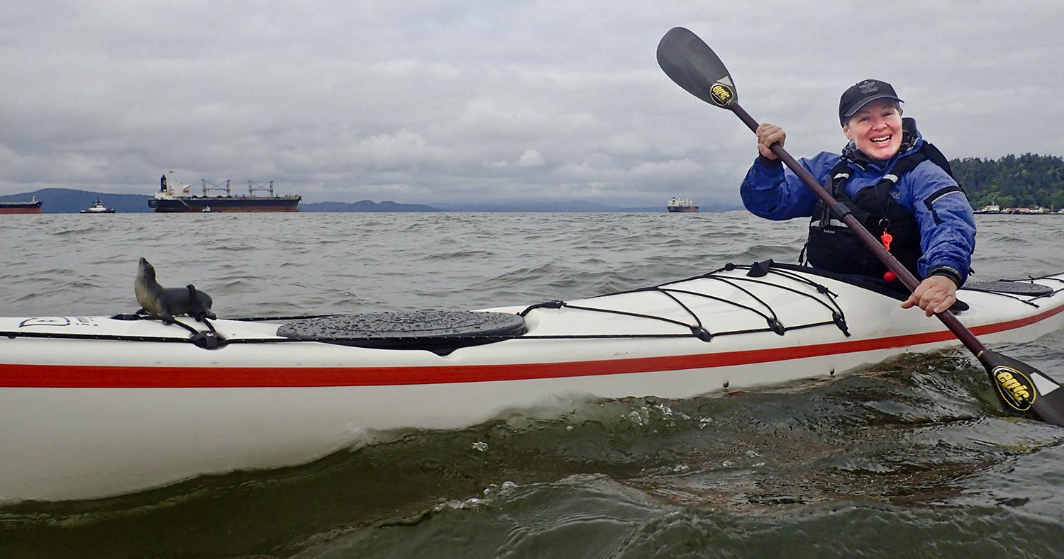 smiling kayaker with cargo ships visible in the distance