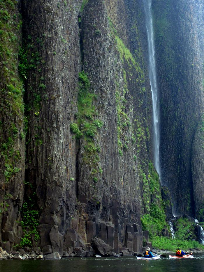 two kayakers are dwarfed by the cliffs and and waterfall on Cape Horn