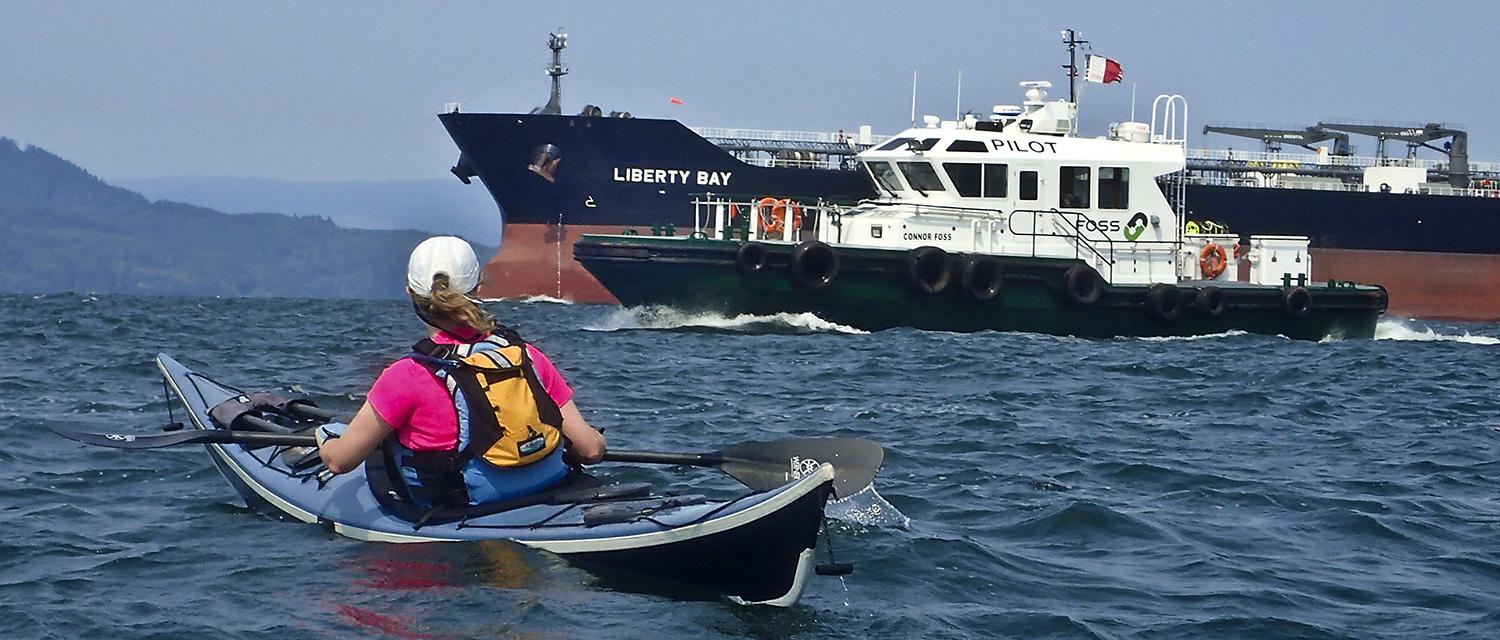kayaker looks toward a cargo ship named Liberty Way, with a Columbia River Bar Pilot ship nearby