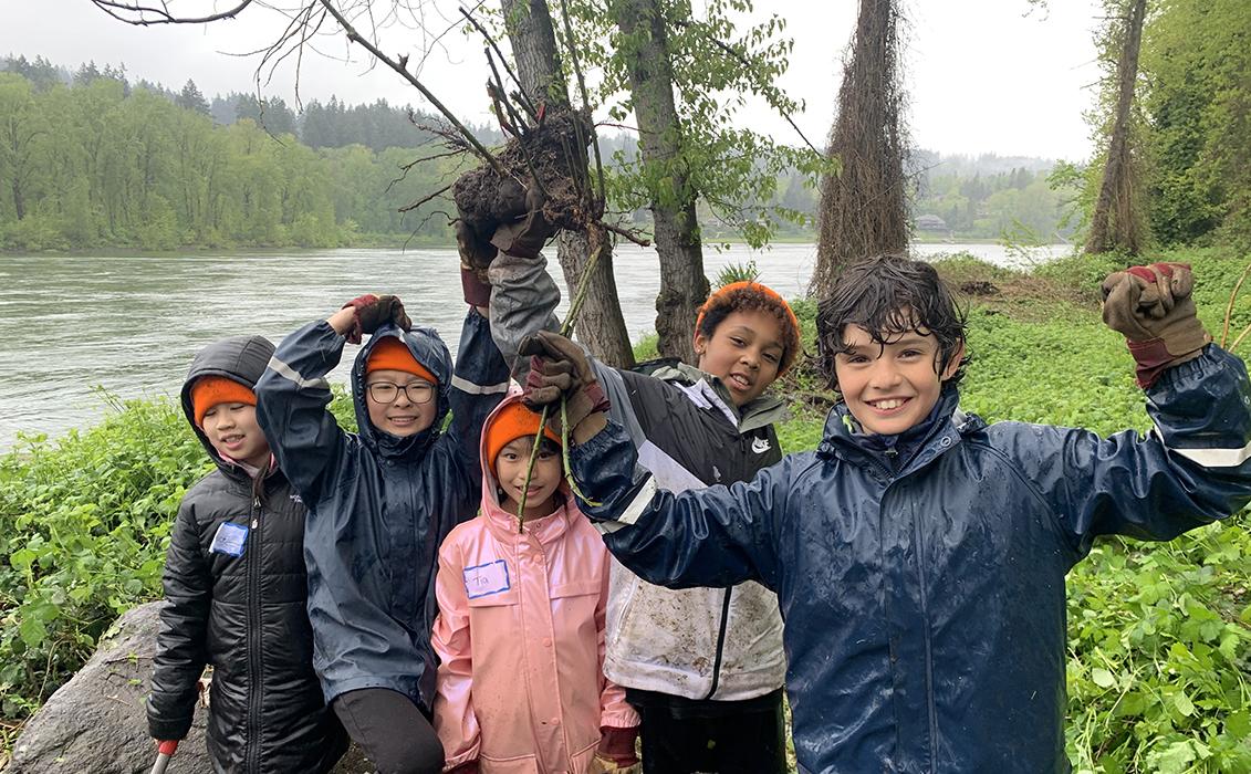 happy students hold up an invasive plant they pulled out by the roots