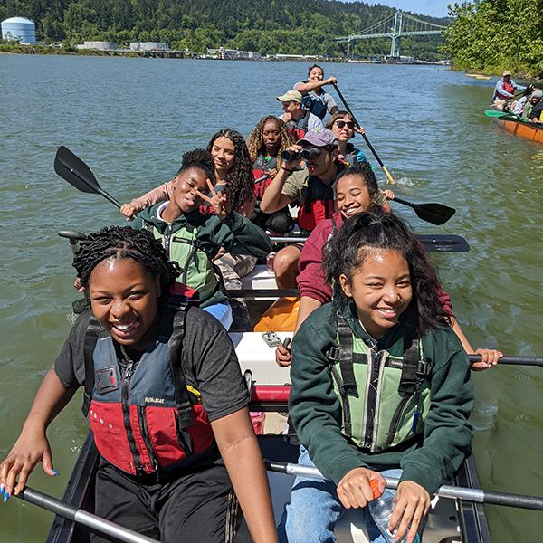 a group happily paddles a big orange canoe