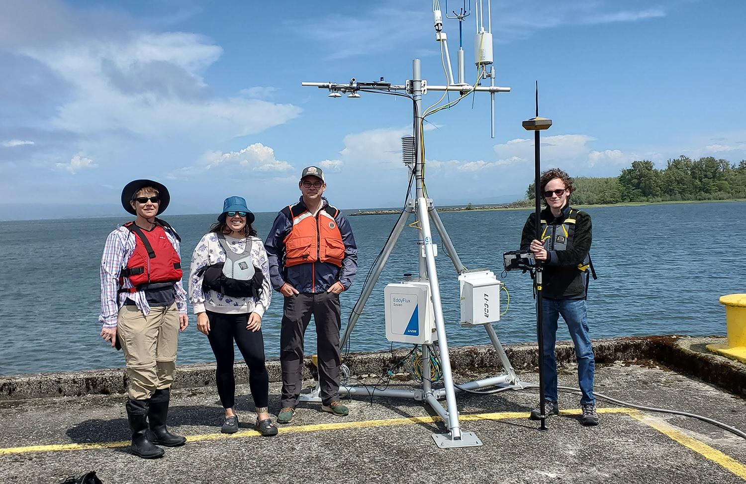 group of four researchers in life jackets stand on a pier by an eddy flux tower