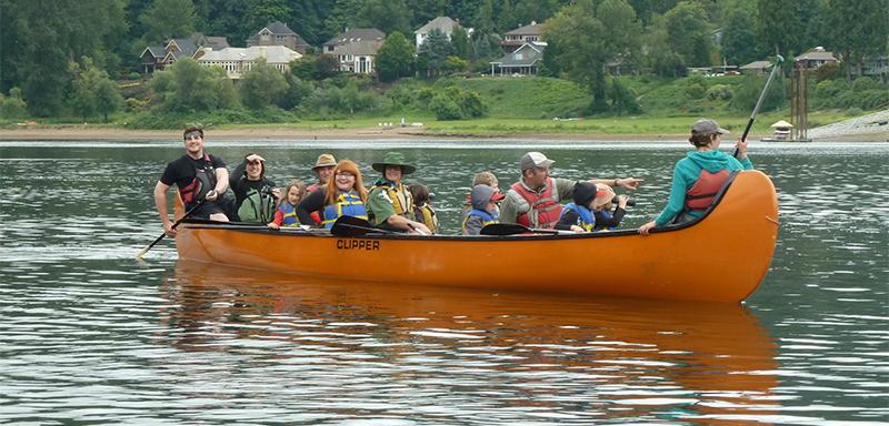 13 people paddle a bright orange big canoe