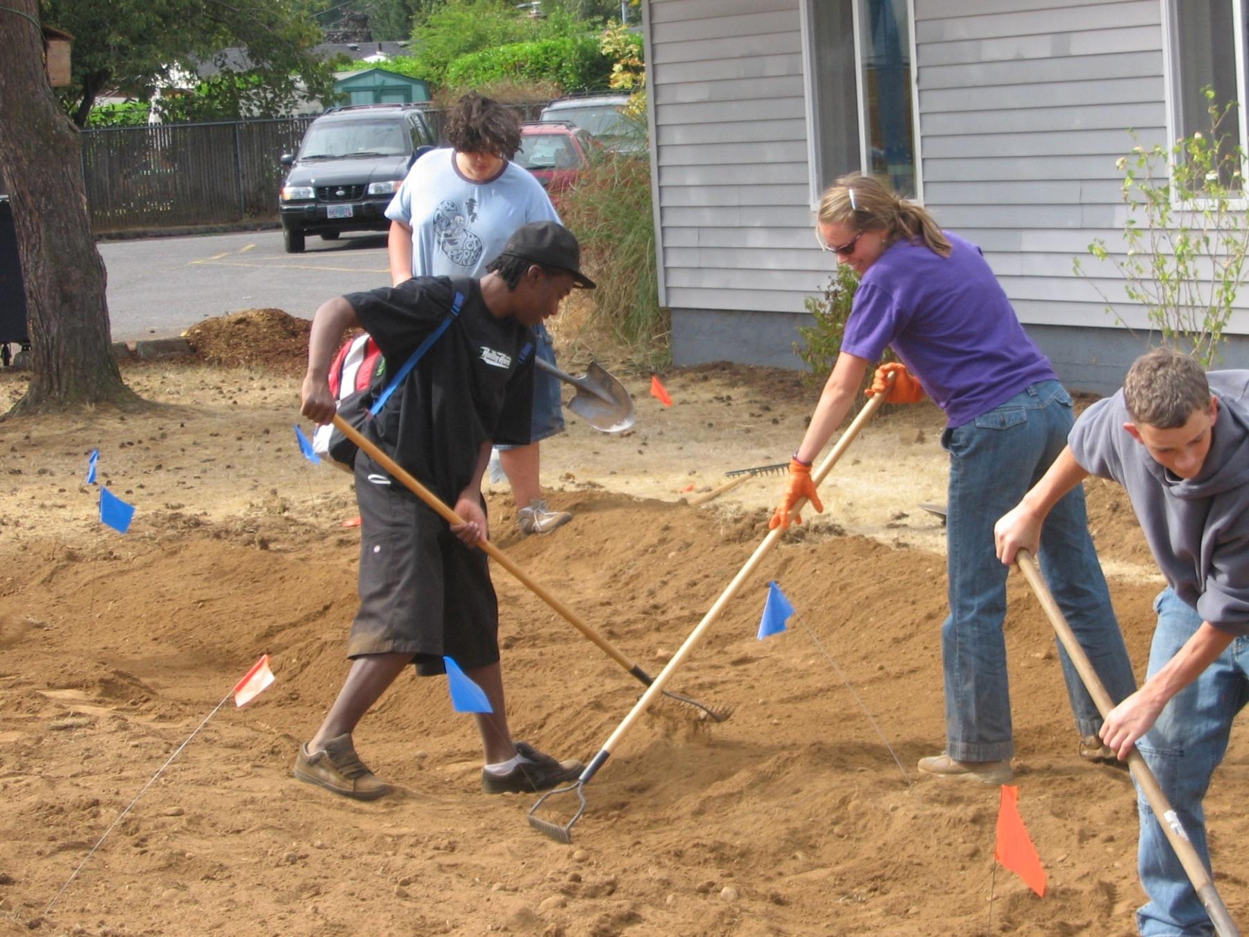 students and staff raking dirt in a stormwater swale under construction