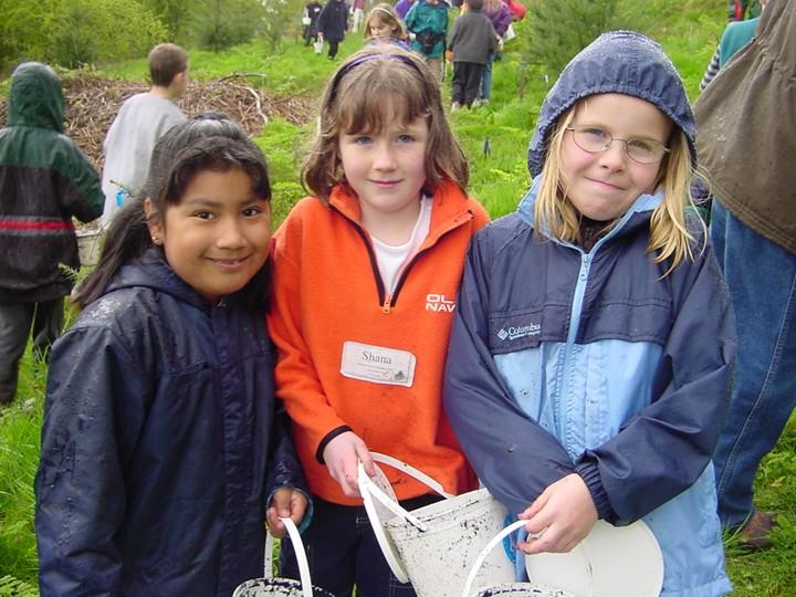 three students stand together outside holding dirty buckets