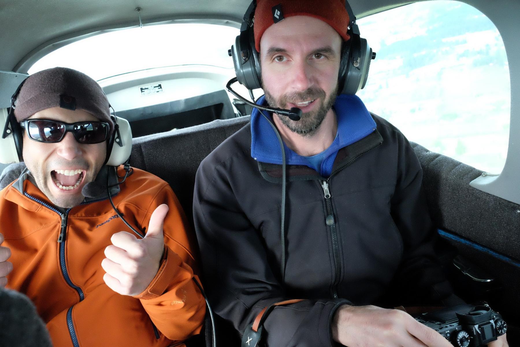 two people in a helicopter with headphones, one giving an enthusiastic thumbs up