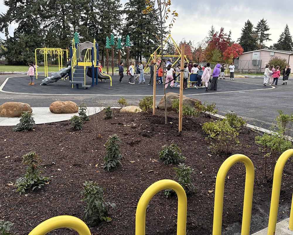 a group of students play on a playgound with a stormwater swale and bike parking in the foreground