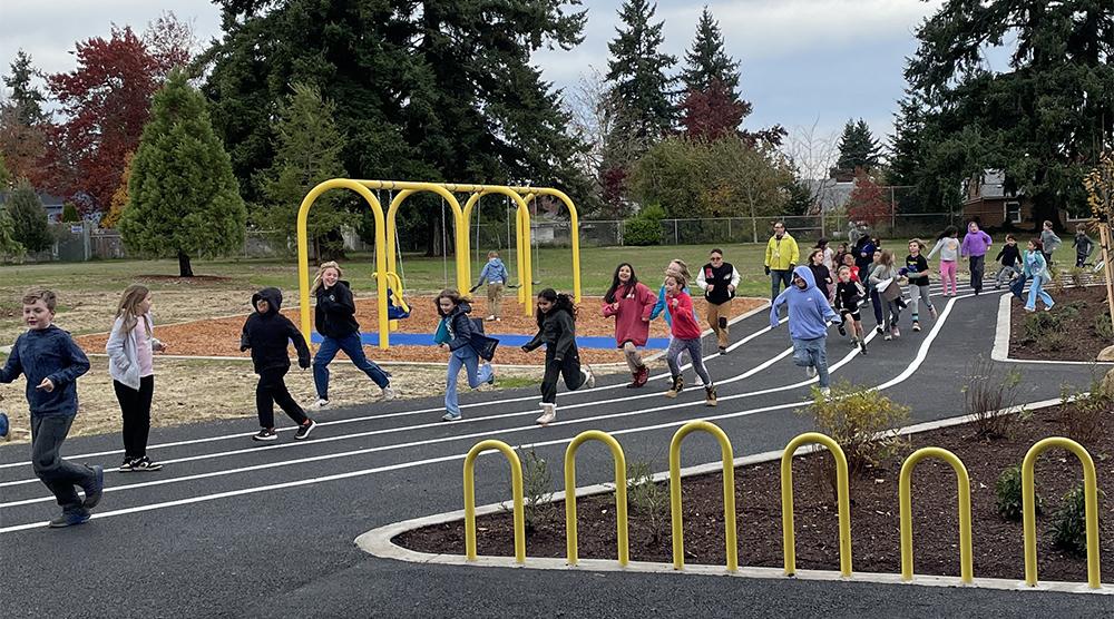 students run around a track surrounding play equipment