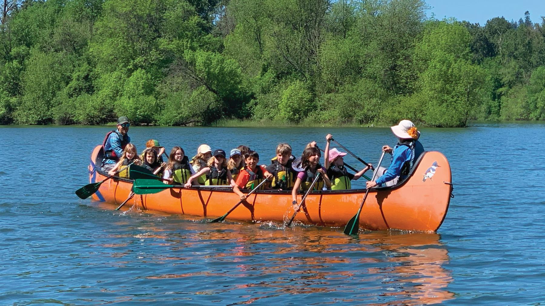 a big orange canoe full of students with adult guides in the front and rear