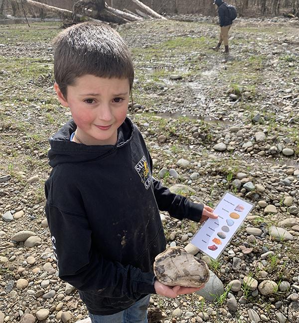 student holds a large rock and a pictorial rock key