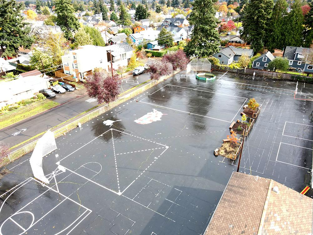 aerial view of the schoolyard shows a large asphalt area with few plants