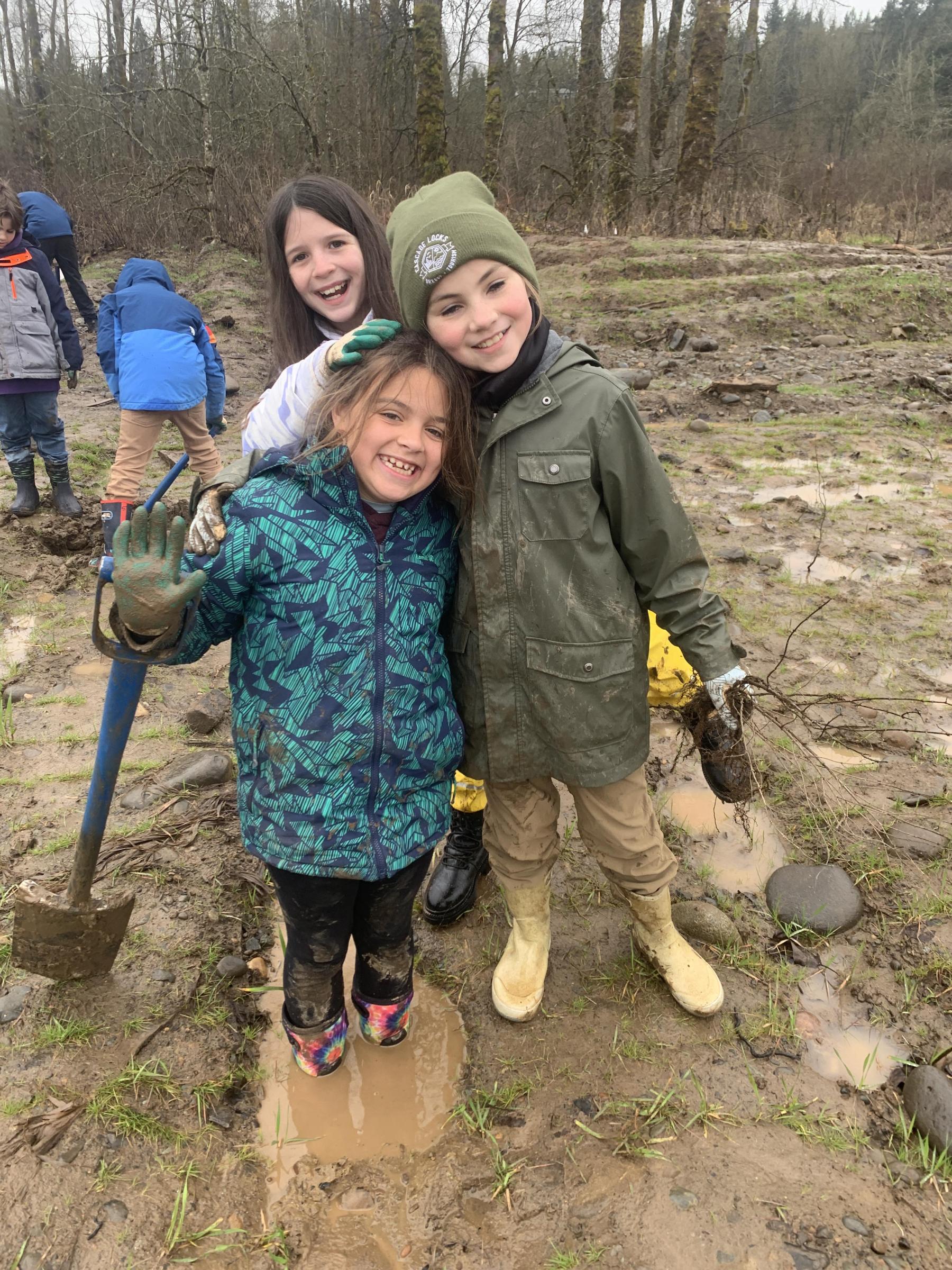 Students embrace each other in the mud while planting trees