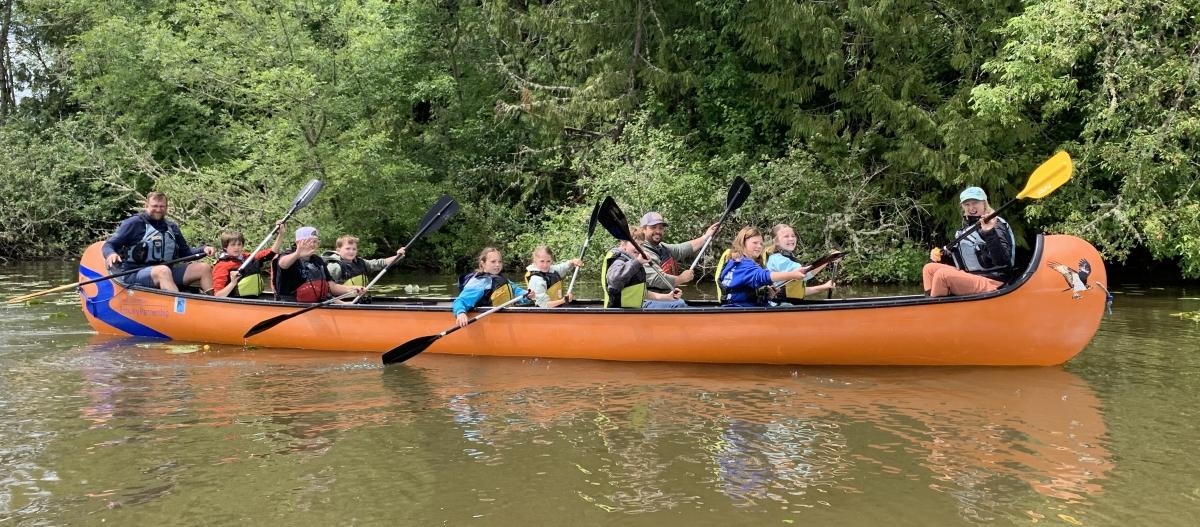 students and guides paddle an orange Big Canoe