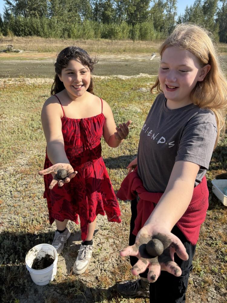 two students hold muddy wapato seed balls