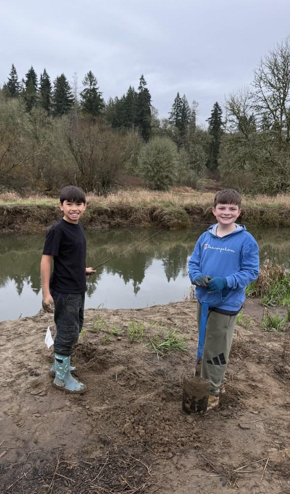 two kids stand by the Salmon Creek while planting shrubs
