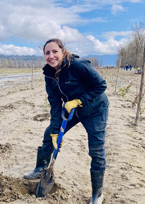 smiling volunteer digs into the muddy dirt. Columbia River visible in the background