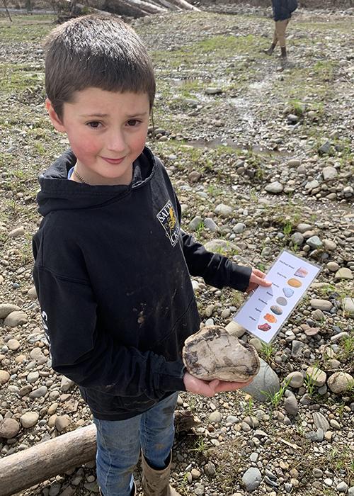 student holds a large rock and a pictorial rock key